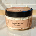 Jar of 'Caramel Kissed Pistachio' whipped body butter on a marble surface with tiled wall background