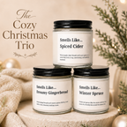 Three candle jars arranged on a stone pedestal with a cozy holiday setup. The top jar reads 'Smells Like.