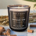 Candle labeled 'Scents of Reverie Midnight Noir' with wooden sticks and lavender on a light surface.