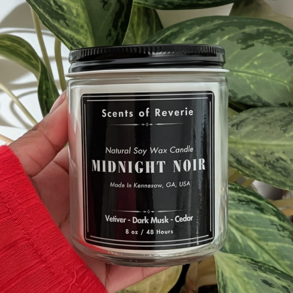 Candle labeled 'Midnight Noir' held in front of a green plant