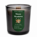A soy wax candle in a smoky translucent dark glass jar with a dark green label reading 'Scents of Reverie Mossy Meadows' and a small wood wick visible at the top, photographed on a white background.