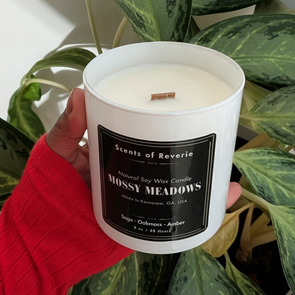 Candle labeled 'Missy Meadows' held in front of a green plant