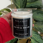 Candle labeled 'Nautical Dream' held in front of a large green plant