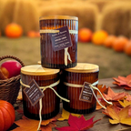 Three small wooden barrels with candles on a wooden table with autumn leaves and pumpkins in the background.
