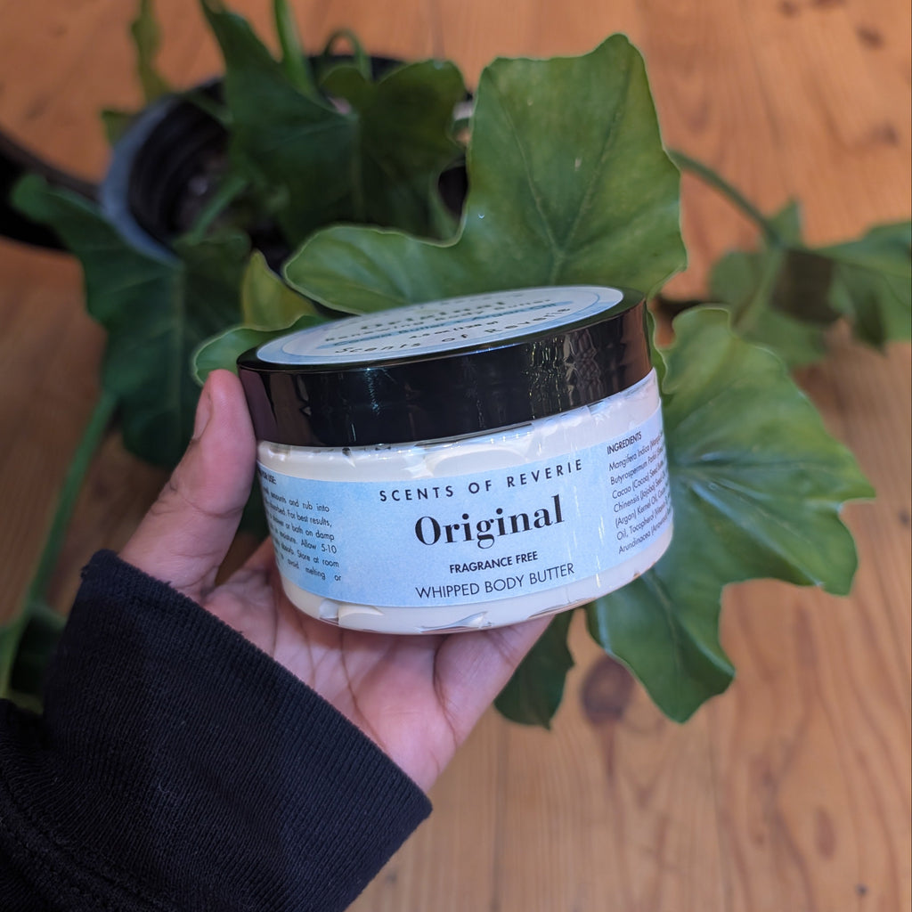Hand holding a jar labeled 'Original' in front of a plant on a wooden floor.