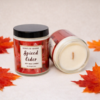 Spiced Cider candle with packaging surrounded by autumn leaves on a light background