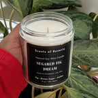 Candle labeled 'Sugared Fig Dream' held by a person with red sleeves, surrounded by green plants.