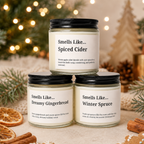 Three scented candles in glass jars are arranged in a holiday-themed setting. The top jar is labeled 'Smells Like.