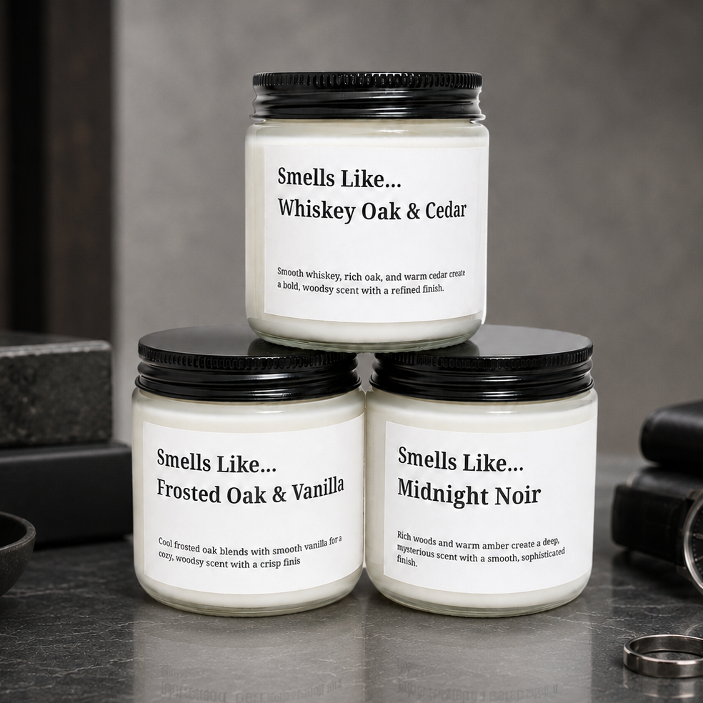 Three scented candles in glass jars with black lids are arranged on a dark stone surface. The top candle reads 'Smells Like.
