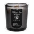 A 7 oz soy wax candle in a dark, translucent smoky gray glass jar with a black label reading 'Scents of Reverie Whiskey Oak & Cedar'.